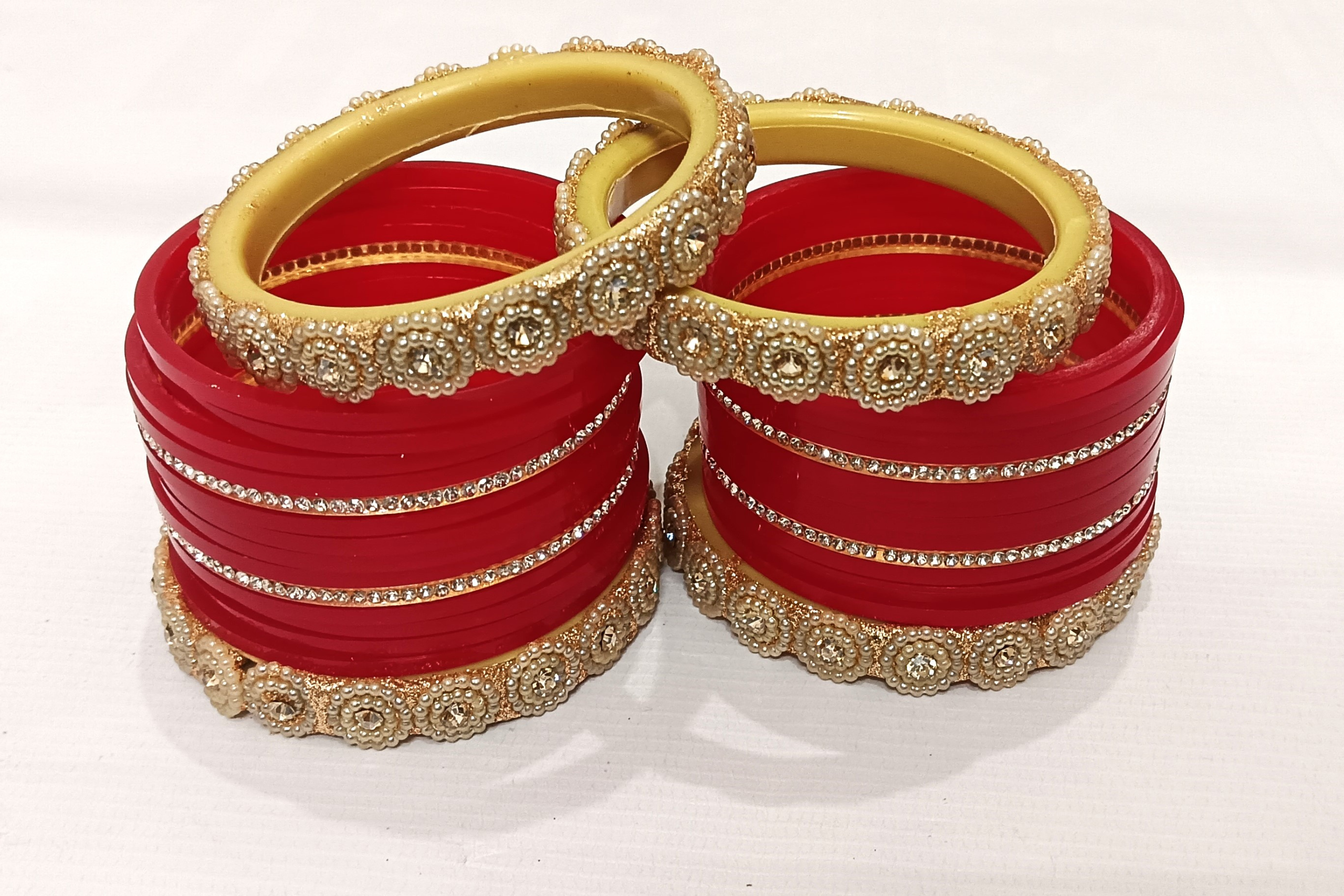 Red bridal chura set with pearl-studded golden kada and rhinestone detailing.